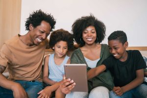 Uma familia composta por 4 pessoas, no meio a mãe segurando um tablet.